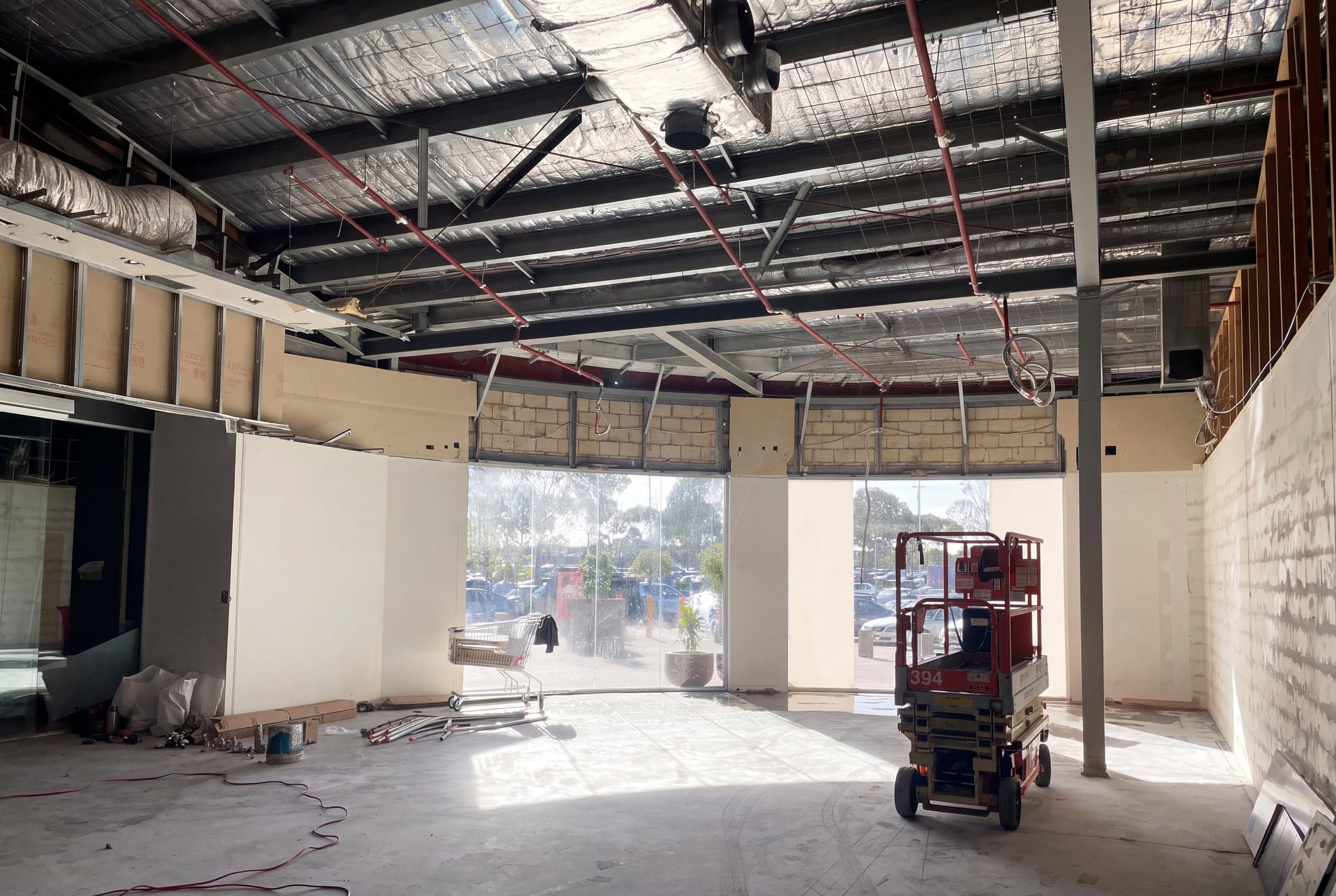 A retail tenancy stripped back for a fit-out, with exposed roof framing, new stud walls and a scissor lift